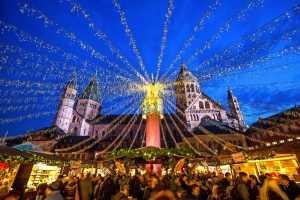Weihnachtsmarkt bei Nacht mit Lichterketten und Kathedrale im Hintergrund.