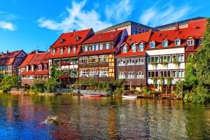 Farbige Fachwerkhäuser am Flussufer unter blauem Himmel.