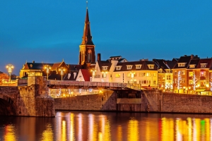 Abendansicht einer Stadt mit Kirche, beleuchteten Gebäuden und Fluss.
