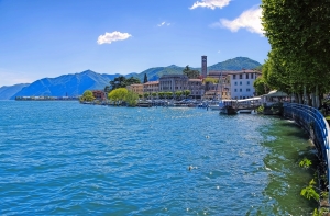 Uferpromenade an einem See mit Gebäuden und Bergen im Hintergrund.