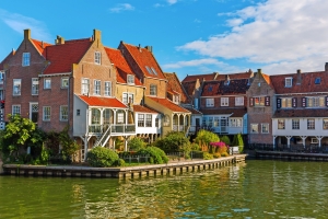 Historische Ziegelhäuser am Wasser in einer malerischen, sonnigen Umgebung.