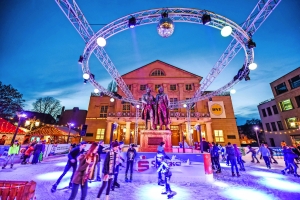 Menschen eislaufen vor beleuchtetem Gebäude in festlicher Atmosphäre auf dem Weimarer Weihnachtsmarkt.