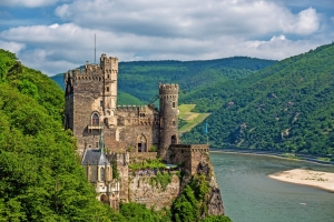 Burg am Fluss mit bewaldeten Hügeln im Hintergrund an einem bewölkten Tag.