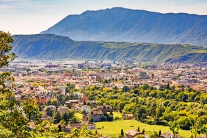 Stadtansicht mit grünen Bäumen und Bergen im Hintergrund bei sonnigem Wetter.