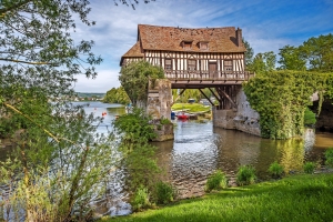 Mittelalterliches Fachwerkhaus auf einer Brücke über einem Fluss, umgeben von Natur.
