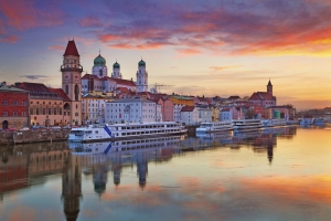 Flussufer einer Stadt bei Sonnenuntergang mit historischen Gebäuden und Schiffen.