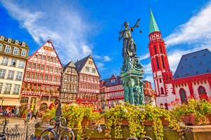 Marktplatz mit Fachwerkhäusern und Justitia-Statue vor blauem Himmel.