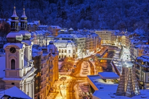 Winterliche Stadtansicht von Karlovy Vary mit beleuchteten Gebäuden und Schnee.