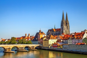 Altstadt von Regensburg mit gotischem Dom und Steinbrücke am Flussufer bei klarem Himmel.