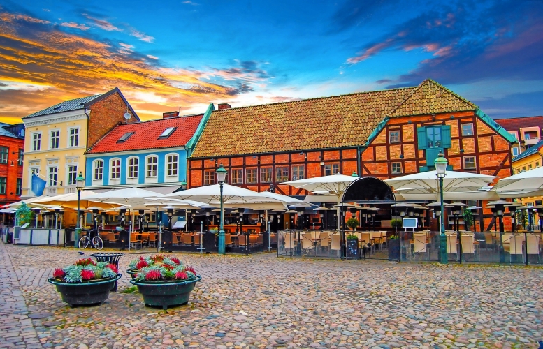 Marktplatz mit Fachwerkgebäuden, Restaurantterrasse und Sonnenschirmen bei Sonnenuntergang.