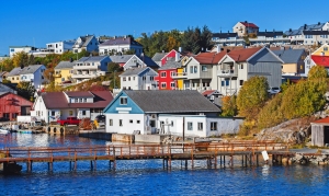 Bunte skandinavische Häuser am Wasser, umgeben von Bäumen und einer Pier im Vordergrund.